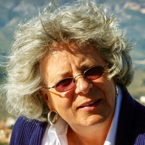 Dawn in a blue cardigan and white shirt, squinting in the sun with the mountains behind her